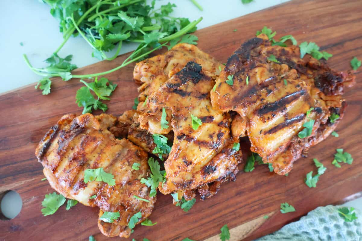3 George Foreman Chicken thighs on a wood cutting board with garnish.
