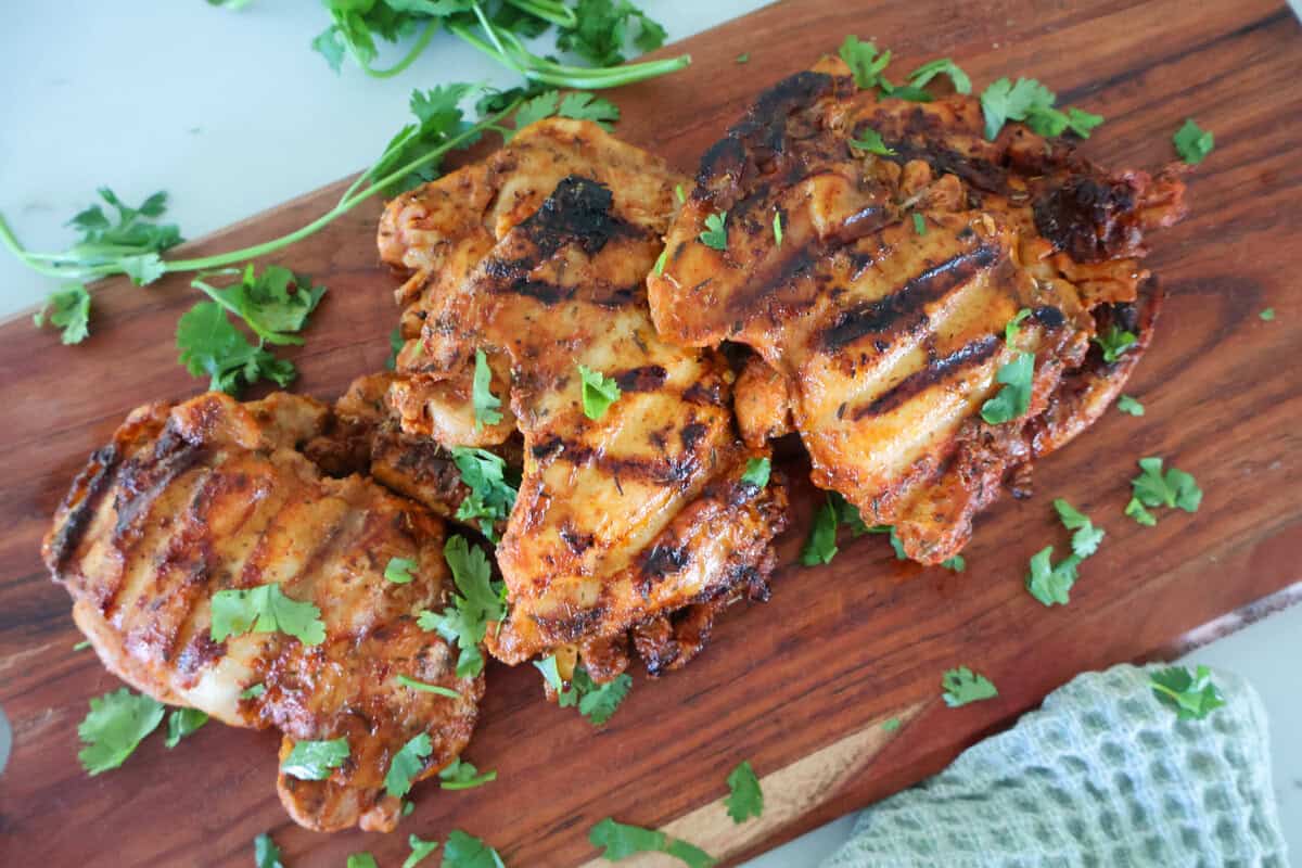 3 George Foreman Chicken thighs on a wood cutting board with garnish.