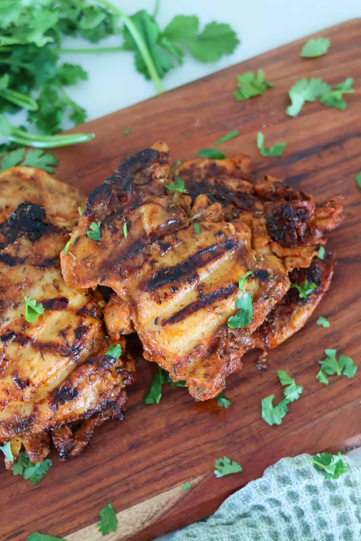 Two George Foreman Chicken Thighs on a wood cutting board with green garnish.