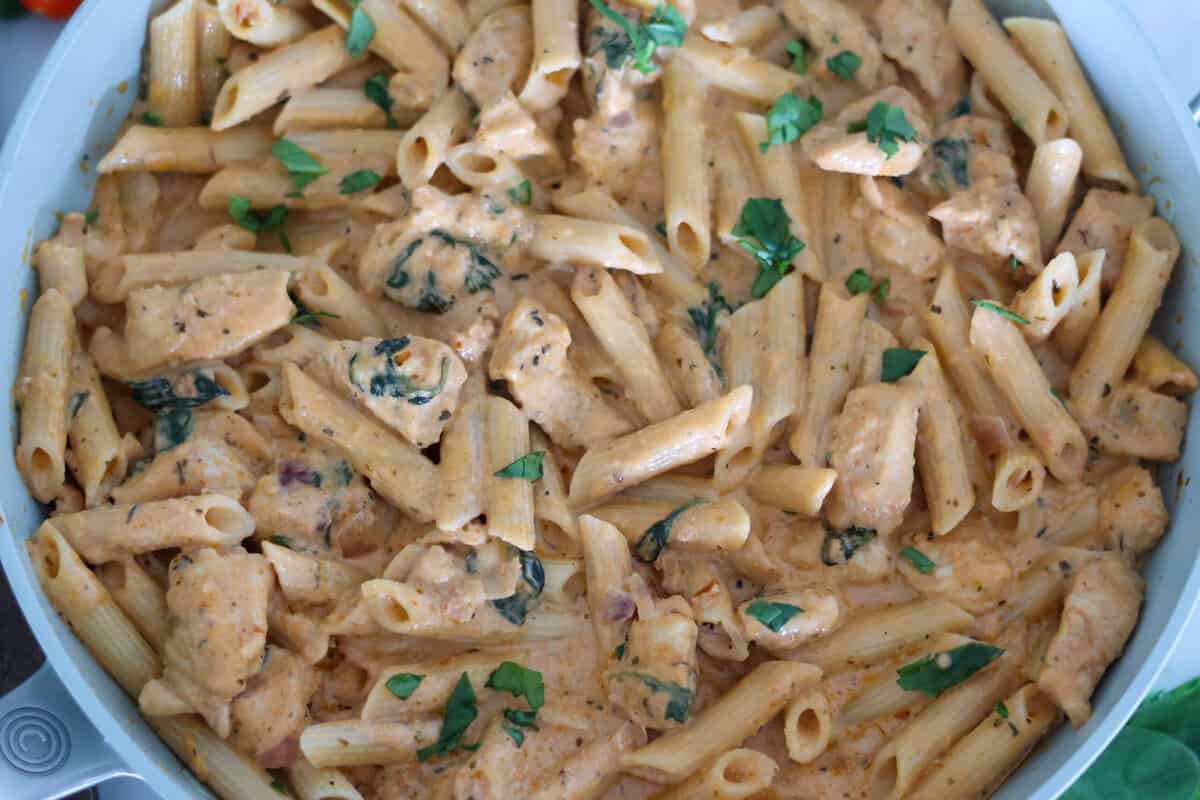 Pesto and Sun Dried Tomato Pasta in a pan with garnish on top.