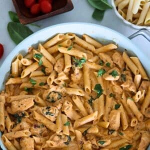Pesto and Sun Dried Tomato Pasta in a pan with garnish on the table.