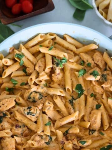 Pesto and Sun Dried Tomato Pasta in a pan with garnish on the table.