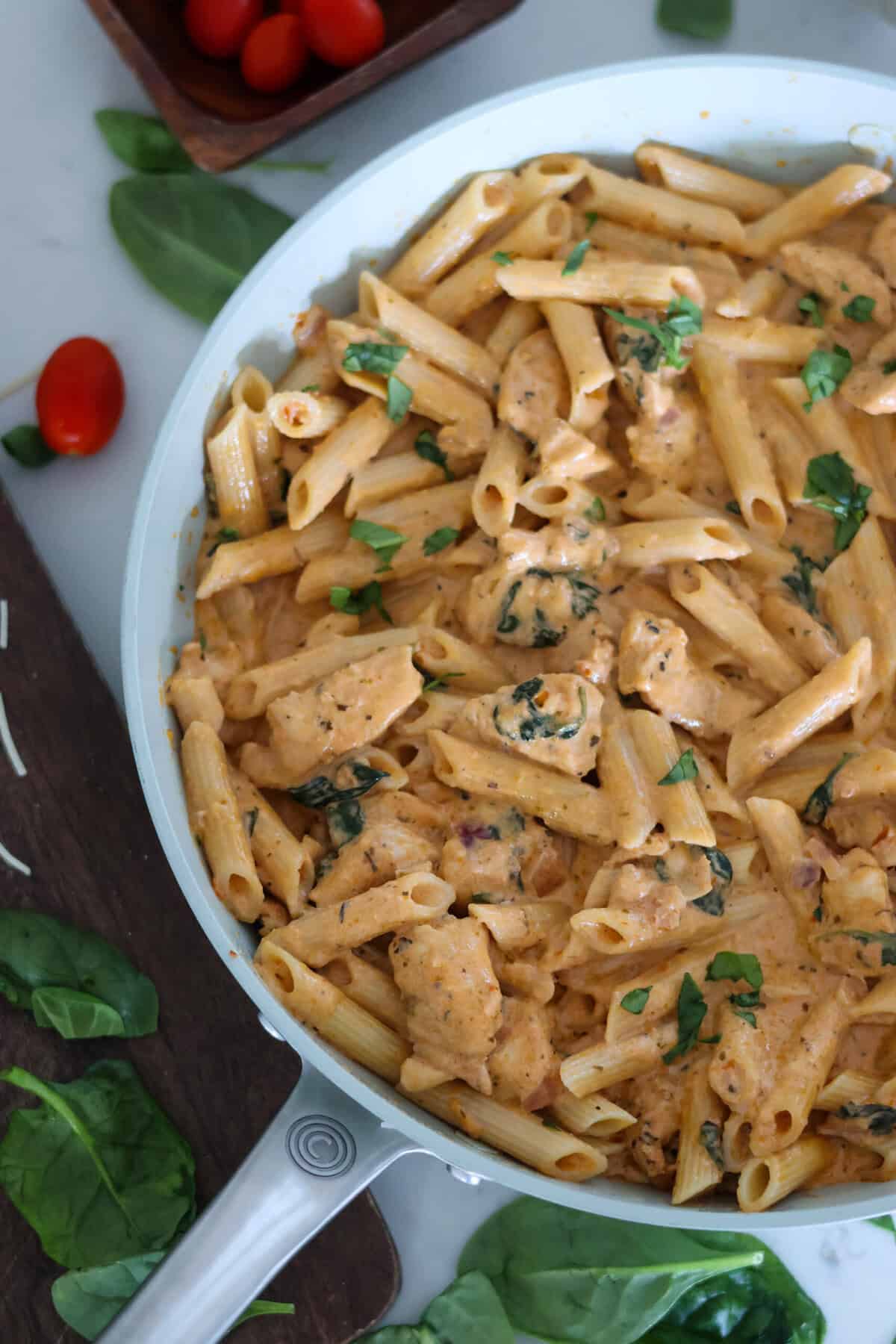 Pesto and Sun Dried Tomato Pasta in a pan with garnish on the table.