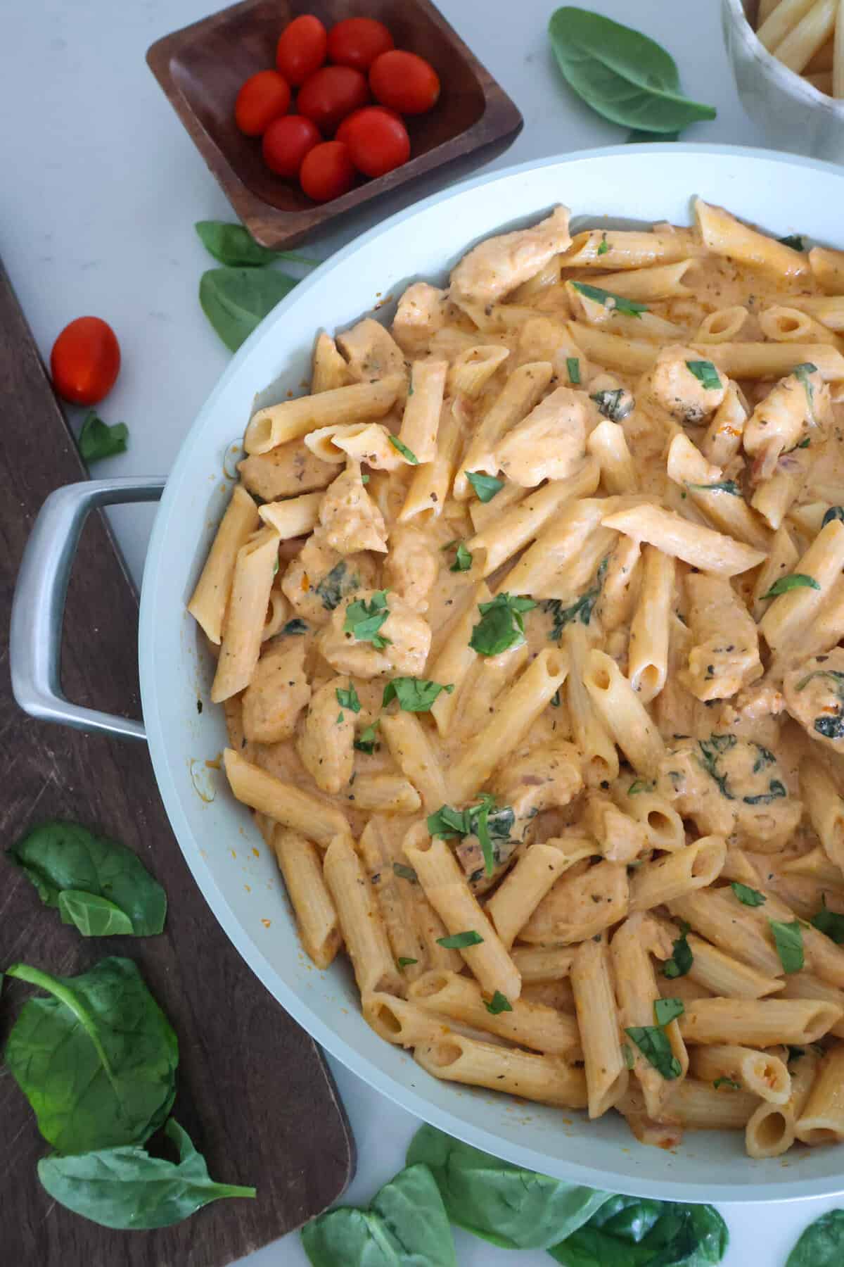 Pesto and Sun Dried Tomato Pasta in a pan with garnish on the table.