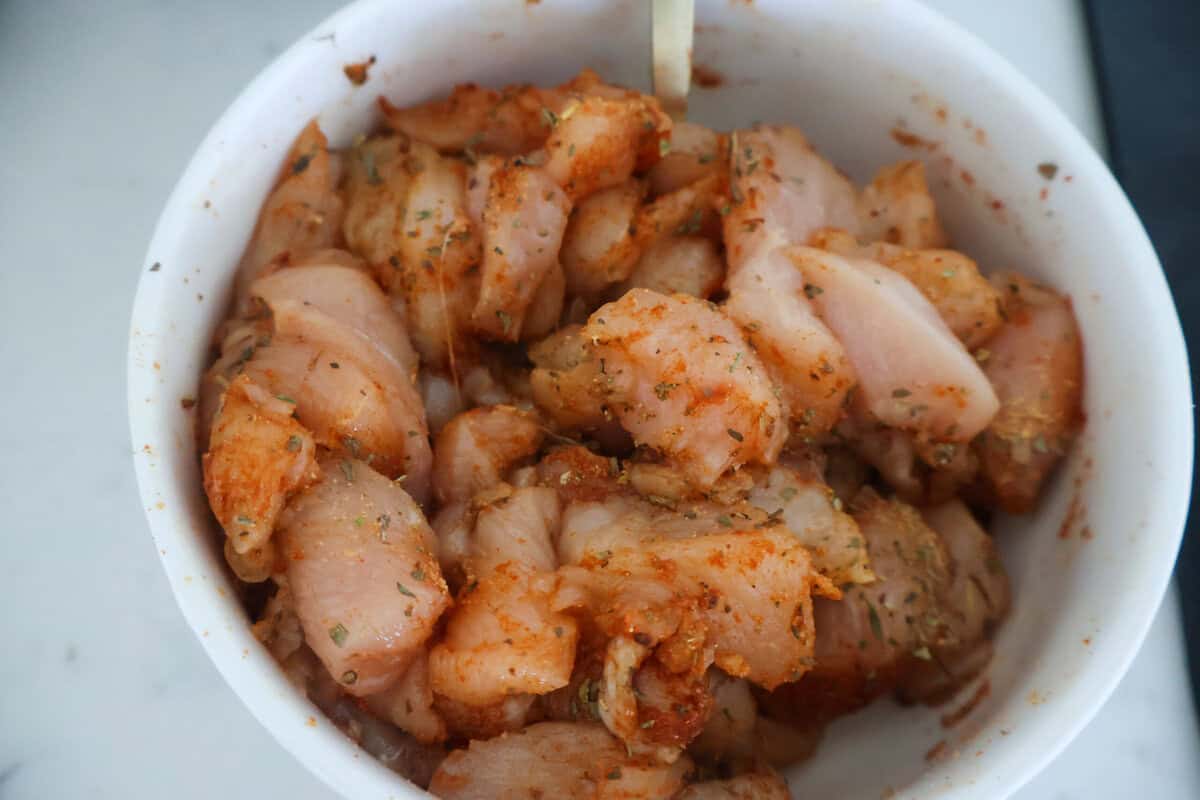 A white bowl of raw seasoned chicken.