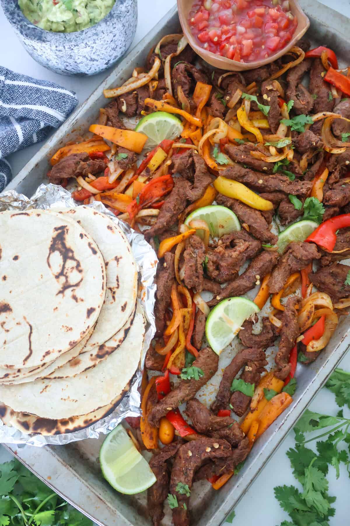 A sheet pan of Steak Fajitas with tortillas and salsa.