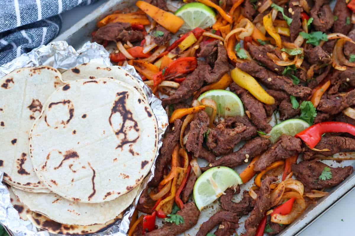 A sheet pan of Steak Fajitas with tortillas and salsa.