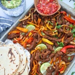 A sheet pan of Steak Fajitas with tortillas and salsa.