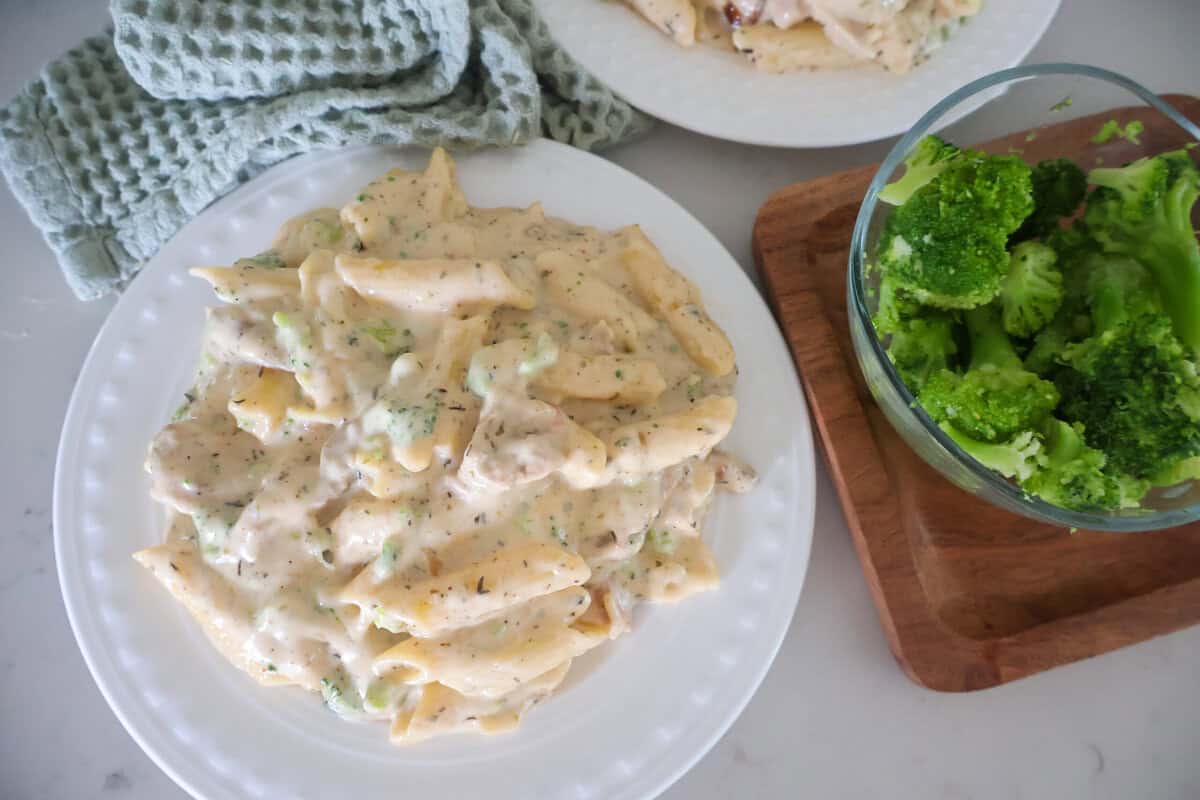A white plate of Chicken Broccoli Penne Pasta with broccoli on the side.