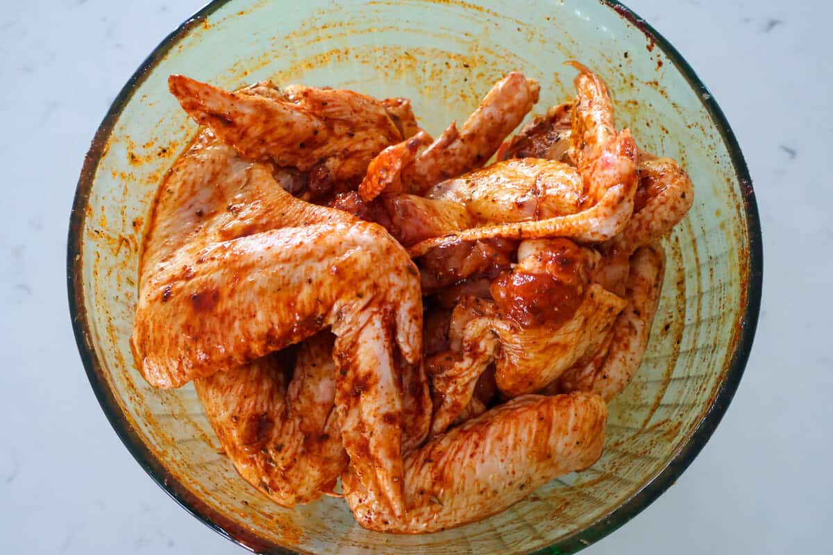 A bowl of marinating raw chicken wings.
