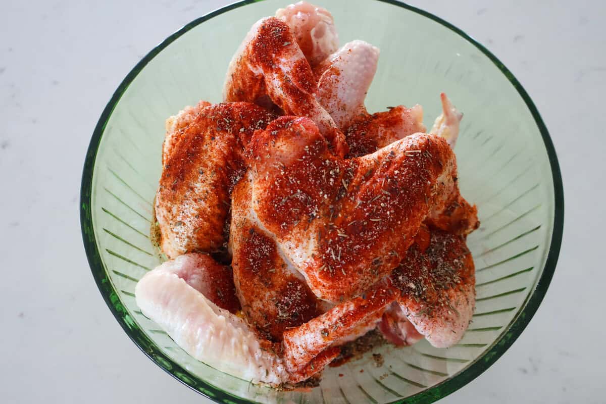 A bowl of raw chicken wings with seasonings on top.