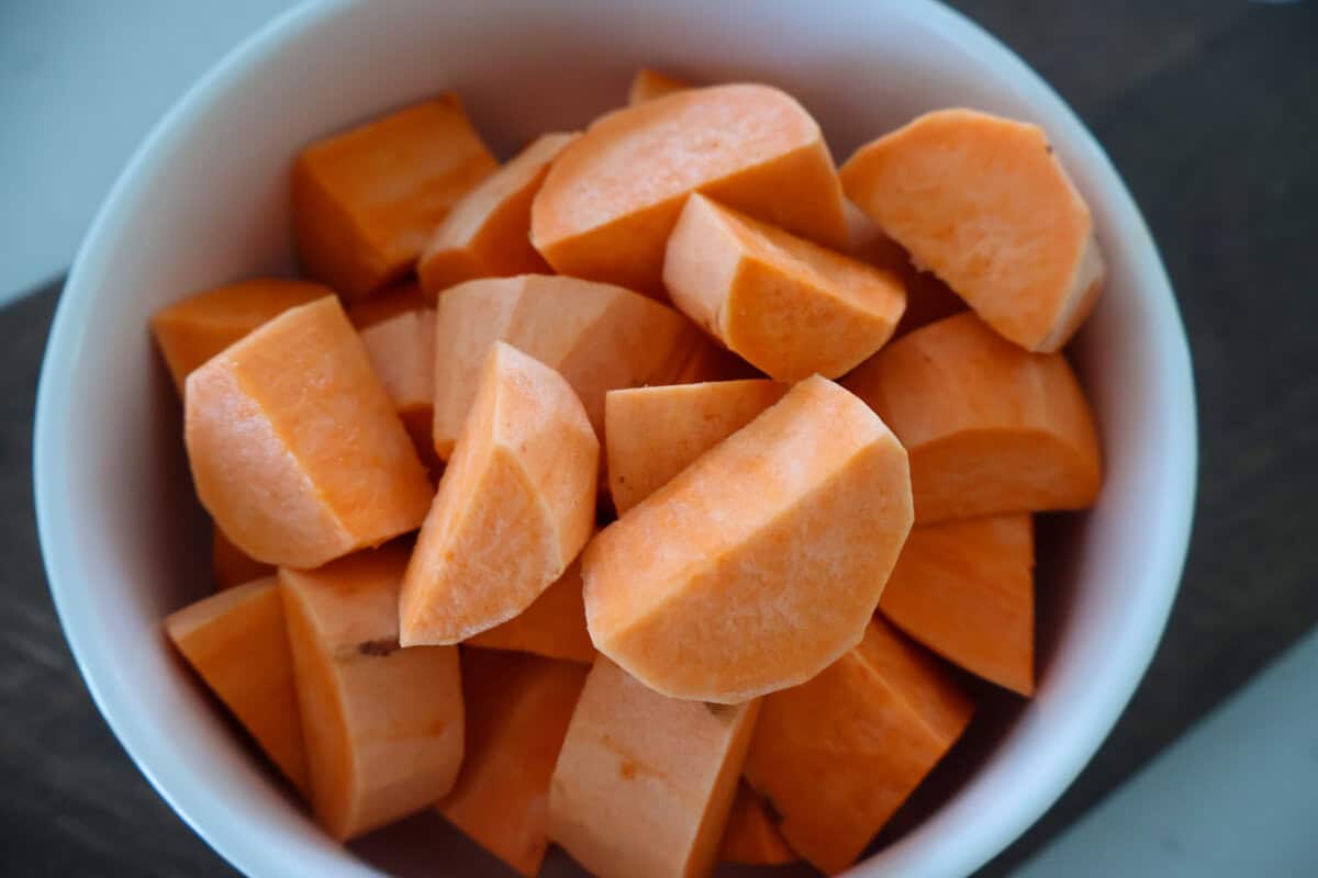 A white bowl of raw sweet potatoes.