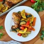 A white plate of sheet pan chicken and vegetables on a cutting board.