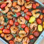 A baking sheet full of cooked shrimp and cherry tomatoes.