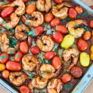A baking sheet full of cooked shrimp and cherry tomatoes.