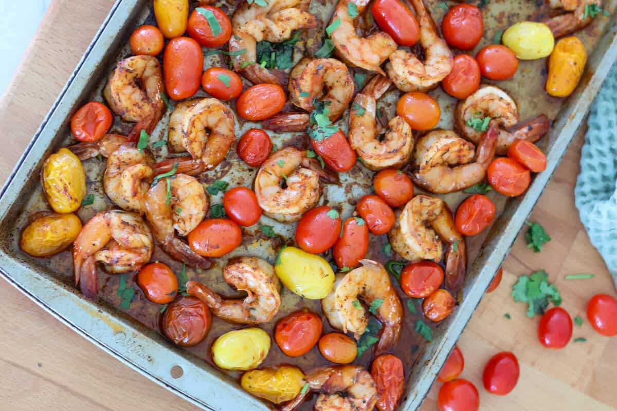A baking sheet full of cooked shrimp and cherry tomatoes.