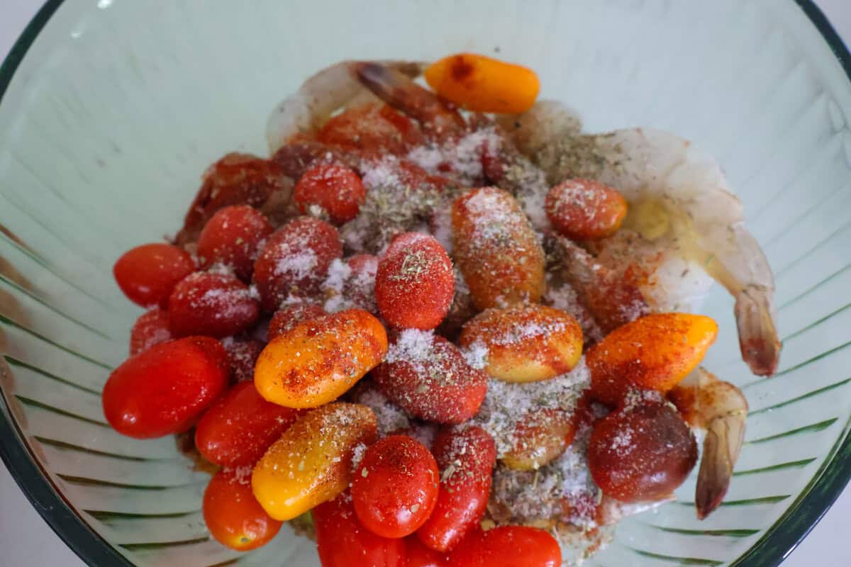 Raw tomatoes and shrimp in a glass bowl with seasonings on top.