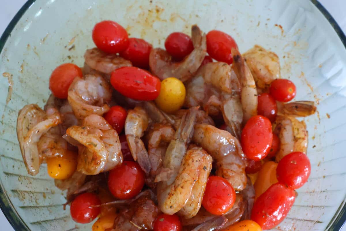 Shrimp and cherry tomatoes marinating in seasoning in a glass bowl.