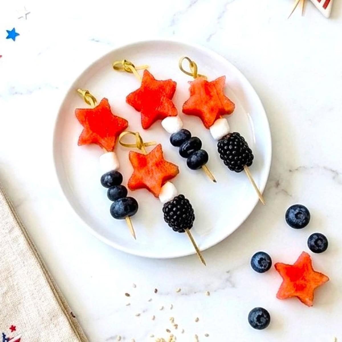 A white plate with watermelon and berry kabobs.