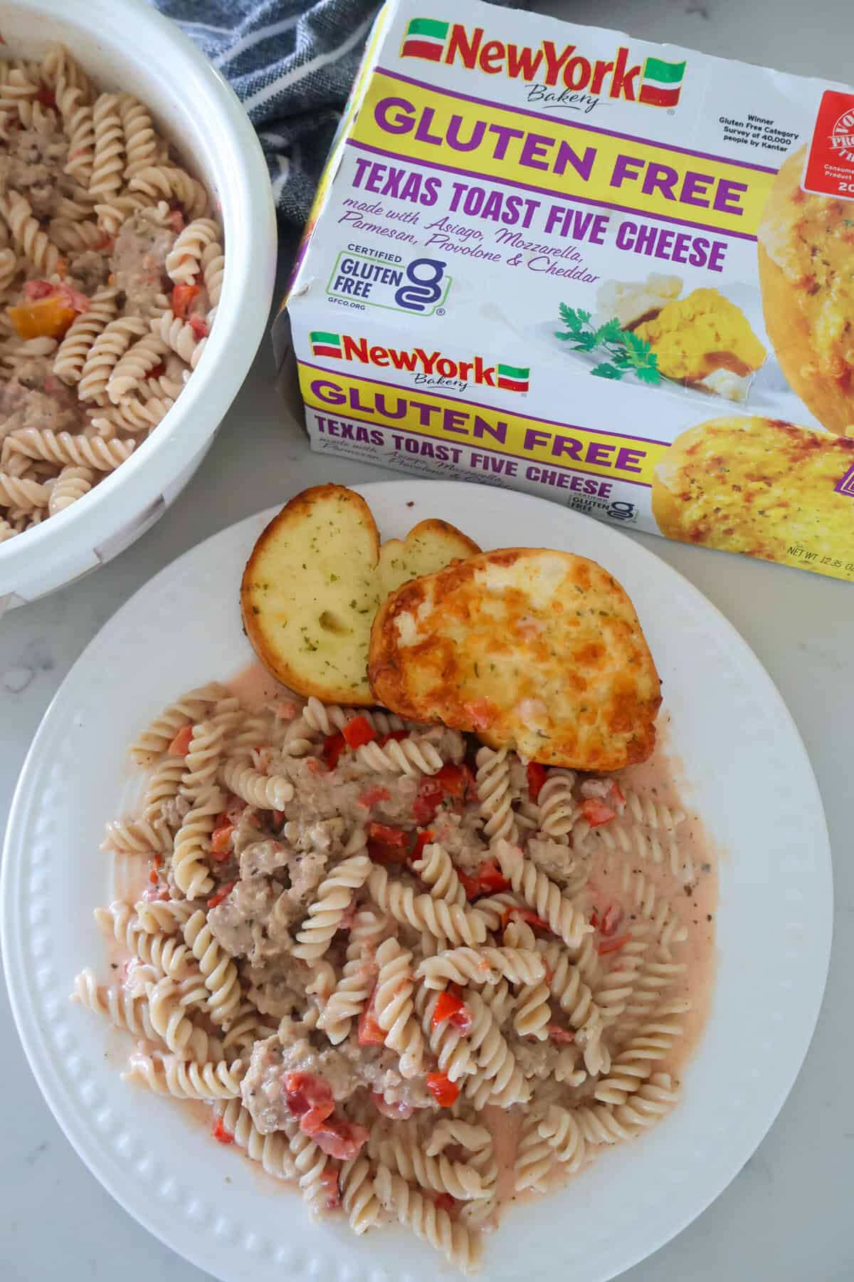 A plate of cream sausage pasta with Texas toast at the top and a box of toast nearby.