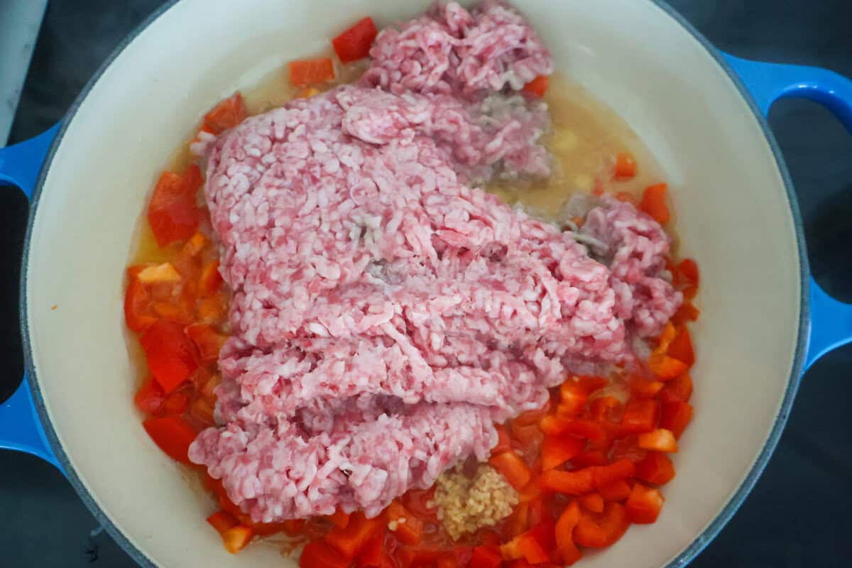 Raw ground sausage, peppers, and oil in a pan to be cooked.