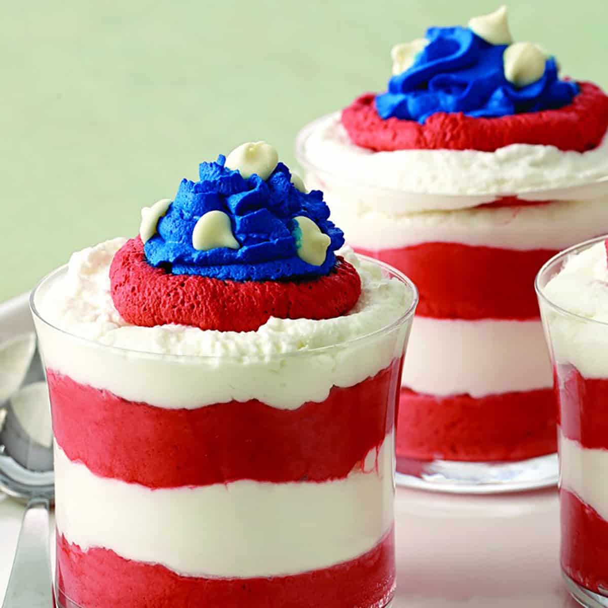 Two red and white mousse parfaits topped with blue frosting.