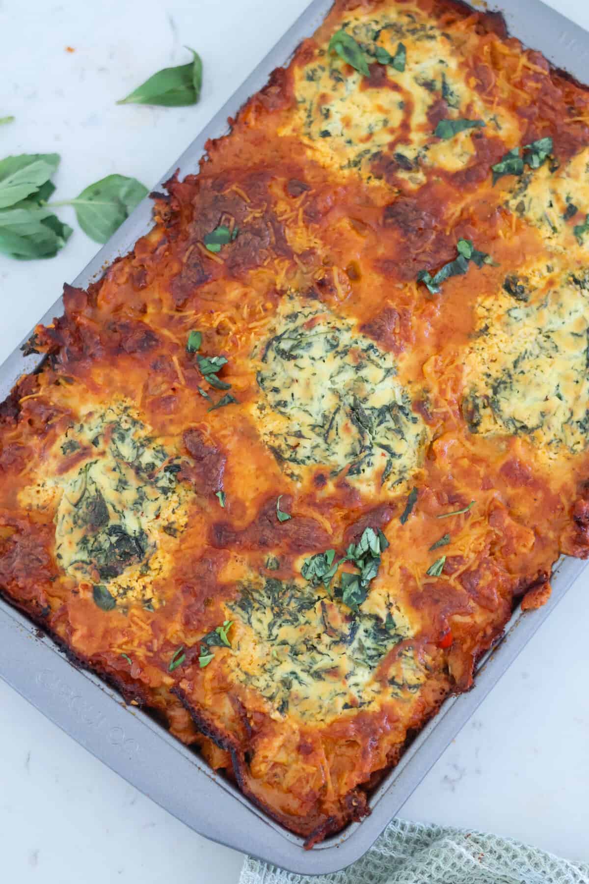 A sheet pan of lasagna with fresh leaves around it.