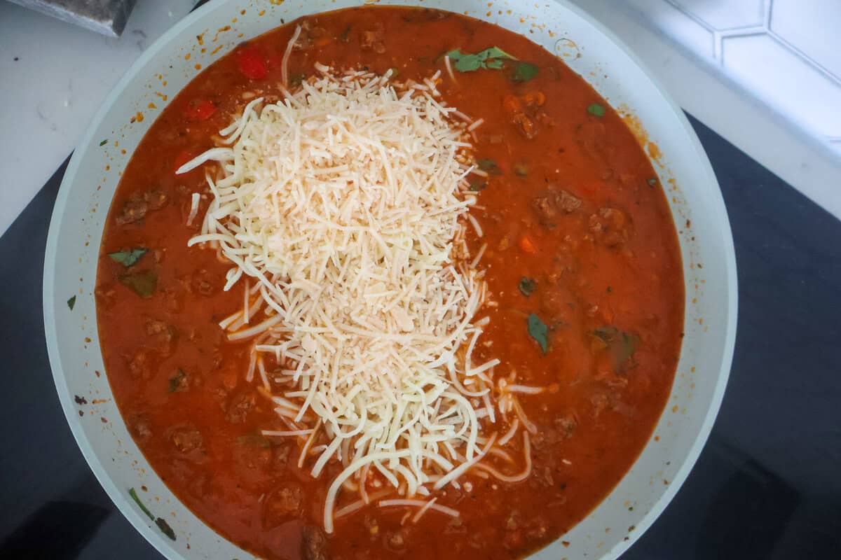 A sauce pan holding a meat sauce and shredded cheese.