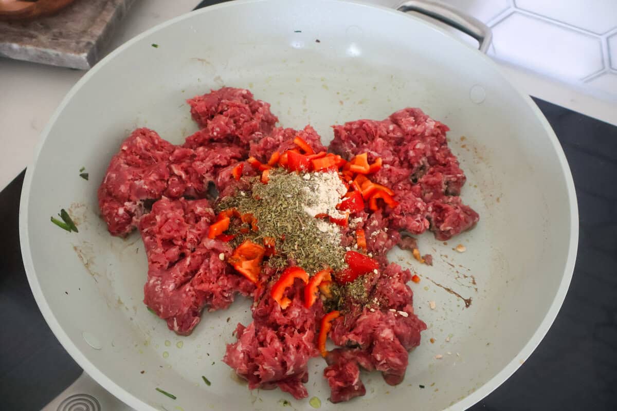 Raw ground beef and spices and red pepper in a pan.