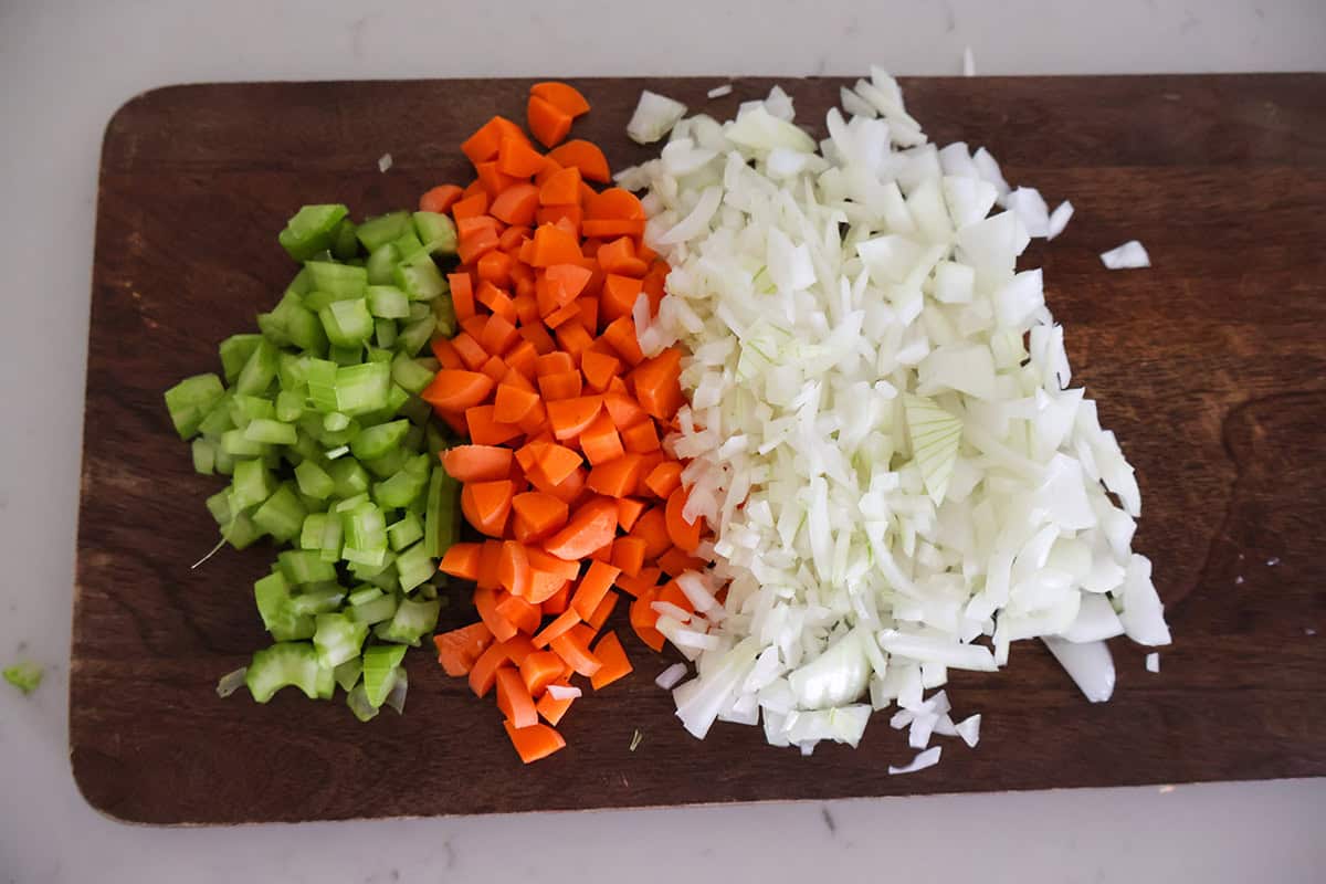 Diced carrots, celery, and onions in columns on a cutting board.