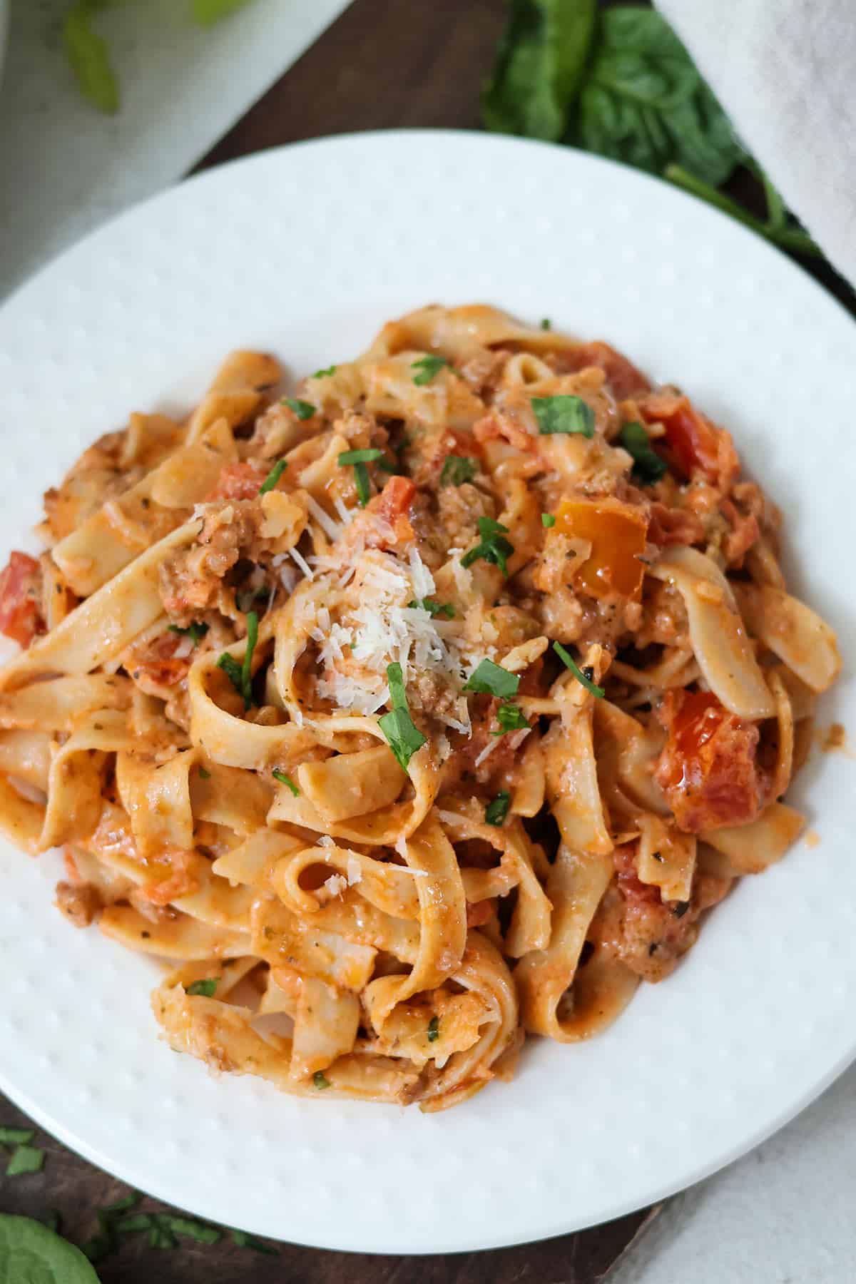 A white plate full of creamy bolognese and pasta.