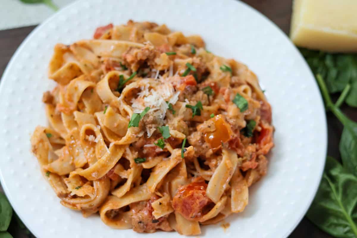 A white plate with creamy bolognese pasta.