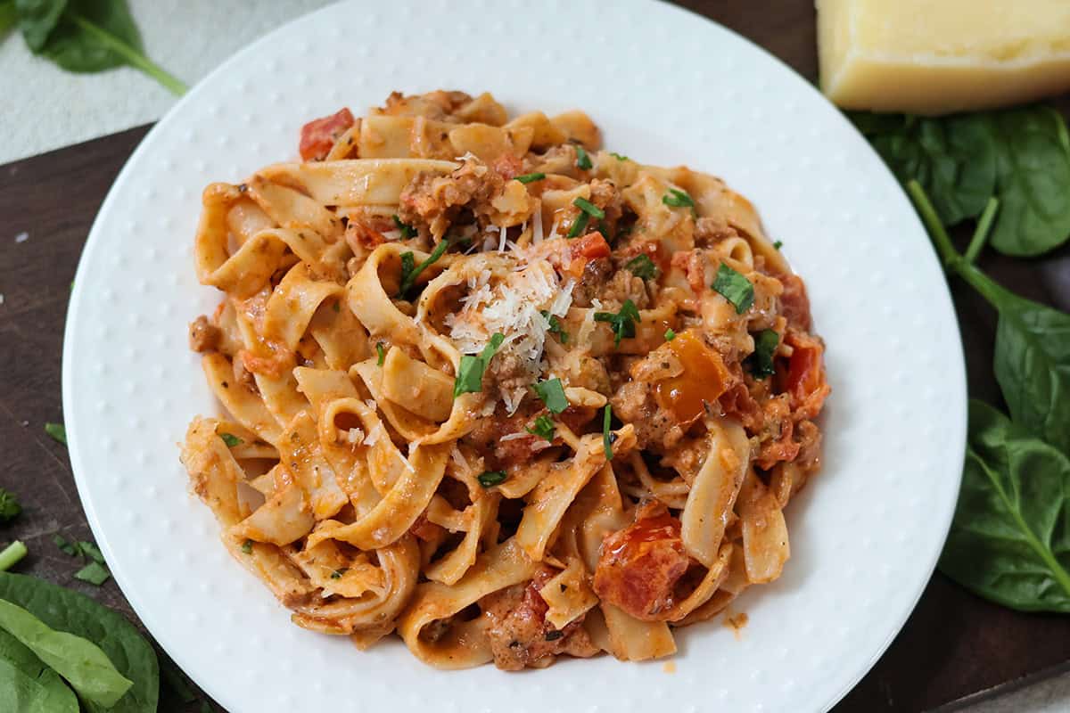 A white plate with creamy bolognese sauce and pasta.
