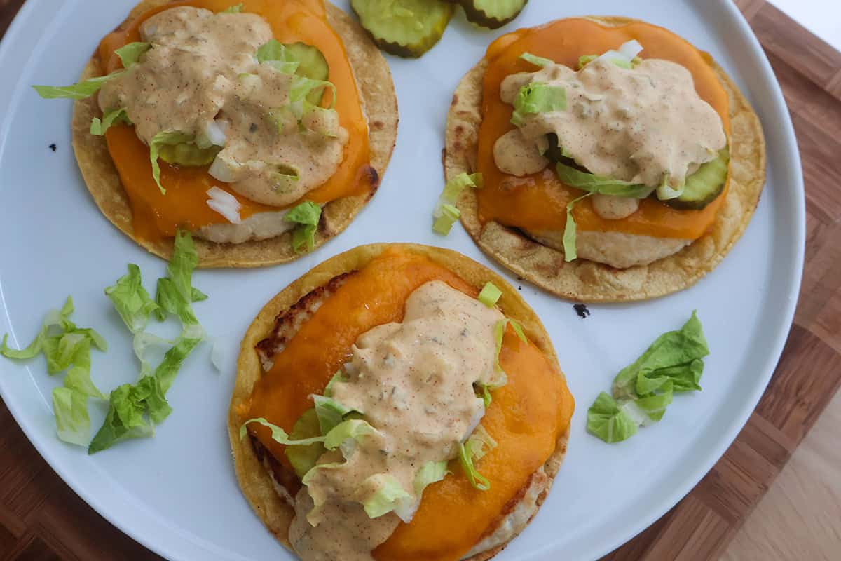 Three chicken smash burger tacos topped with sauce on a white serving plate.