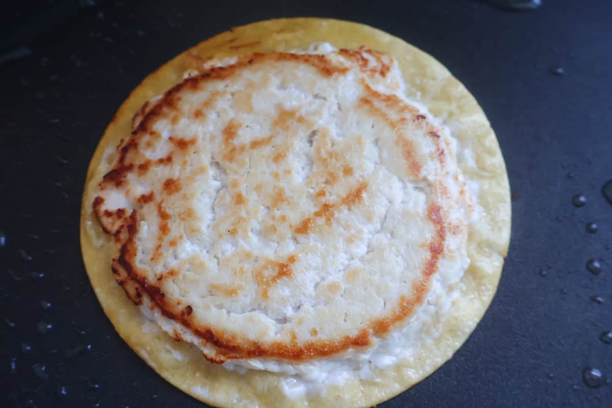 A cooked smashed chicken burger on a tortilla.