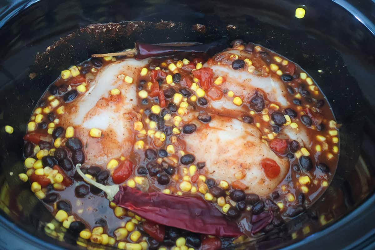 Raw chicken, beans, corn, and chiles in broth in a crock pot.