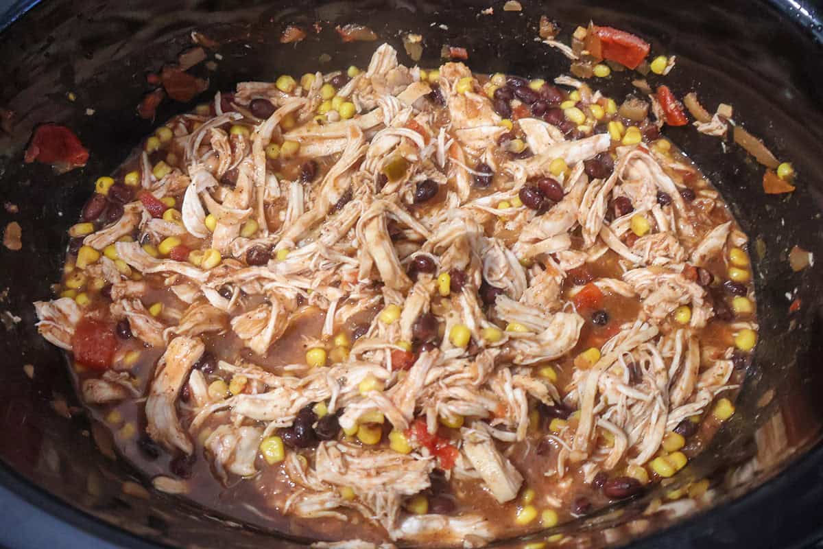 A crock pot full of shredded chicken, beans, and corn.