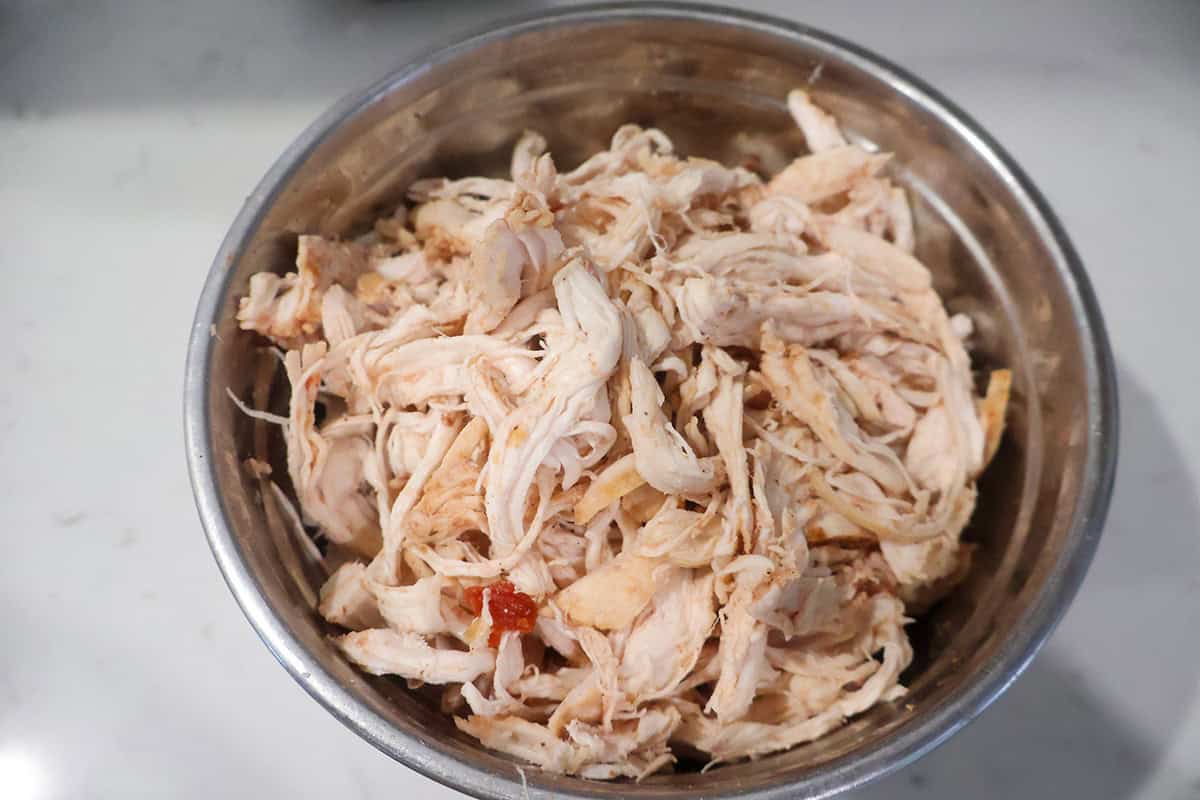 A metal bowl filled with shredded chicken.
