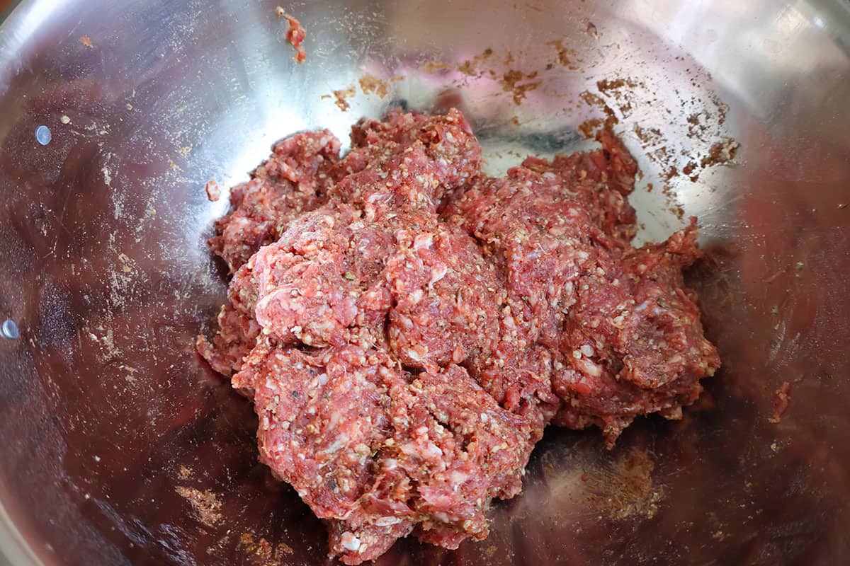 Seasoned ground beef meatball mixture in a metal mixing bowl.