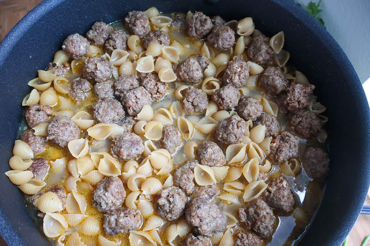 A skillet full of browned mini meatballs and pasta shells.
