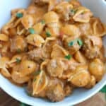 A white bowlful of mini meatballs and shells in sauce.