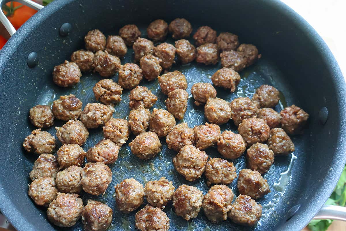 A skillet filled with browned mini meatballs.