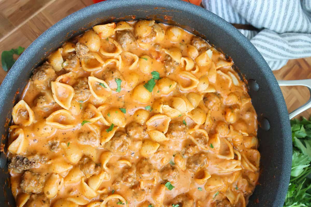 A skillet full of creamy pasta with mini meatballs.