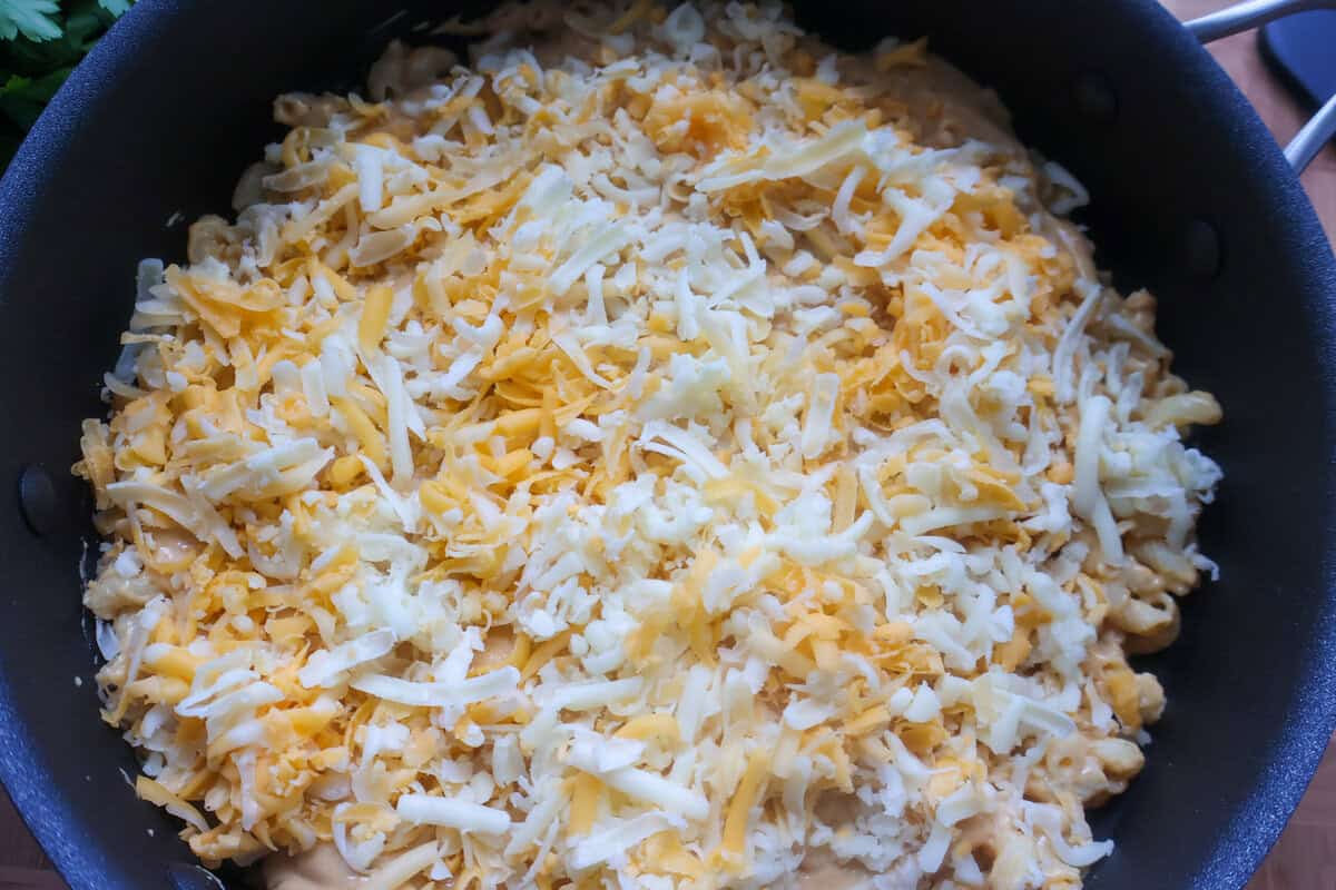 A skillet of raw mac and cheese with a layer of cheese on top in a black skillet.