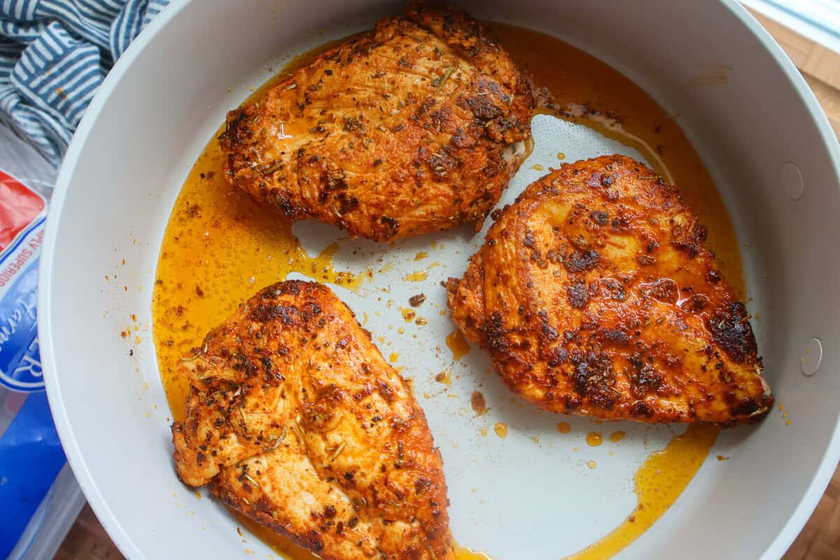 A pan of cooked chicken breasts in oil.