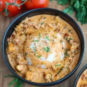 A black bowl of Marry Me Chicken atop white rice with tomatoes on the side.