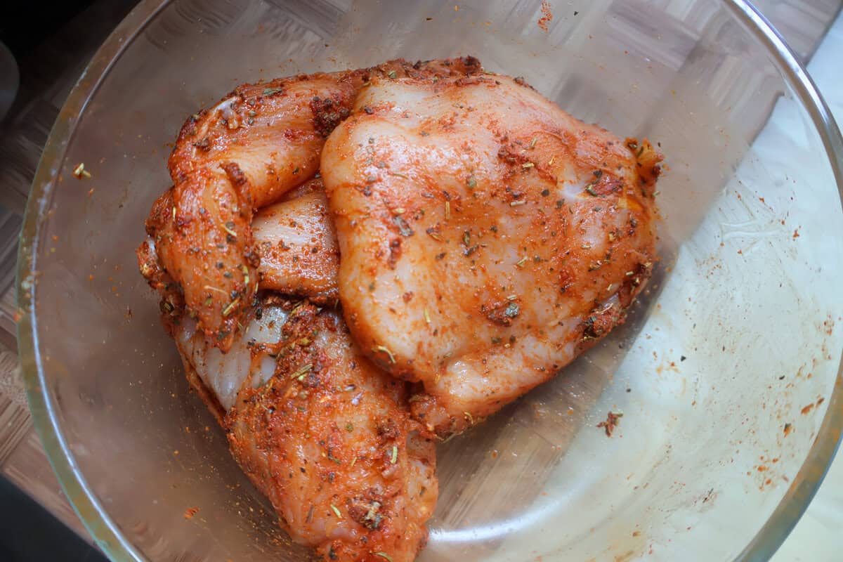 Seasoned chicken breasts in a glass bowl marinating.