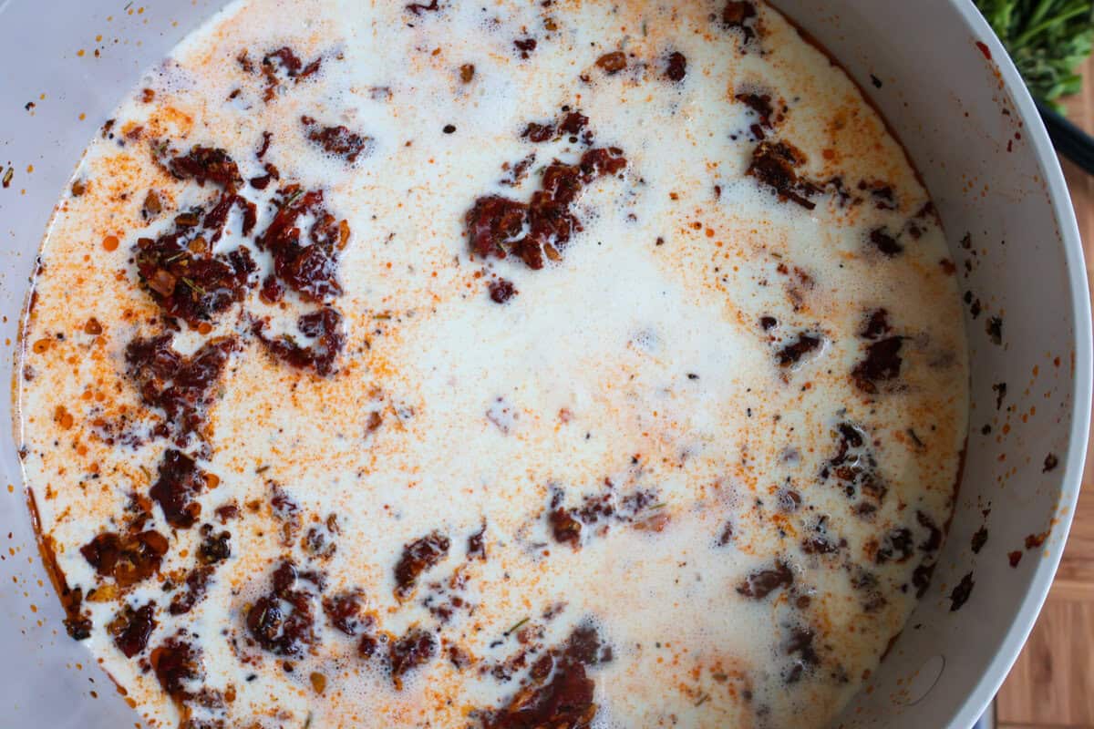 Heavy cream mixing with a blend of seasonings to make a cream sauce in a skillet.