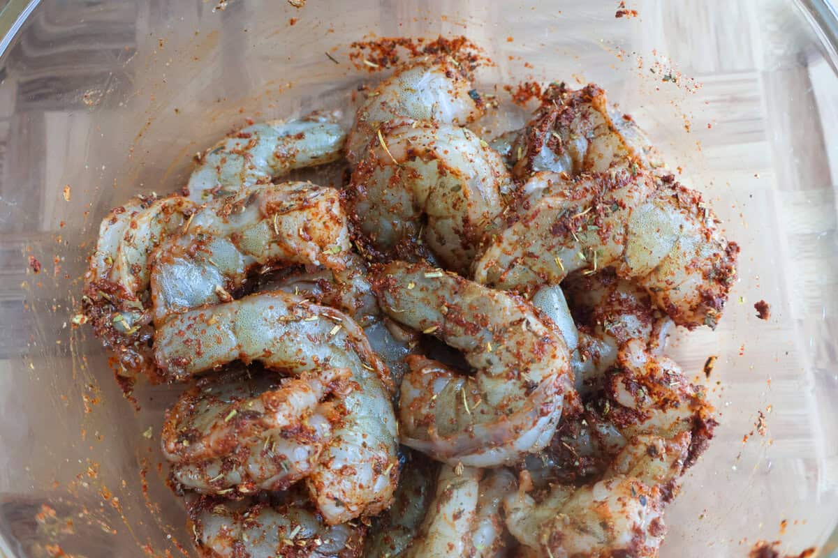 A glass bowl full of raw seasoned shrimp.