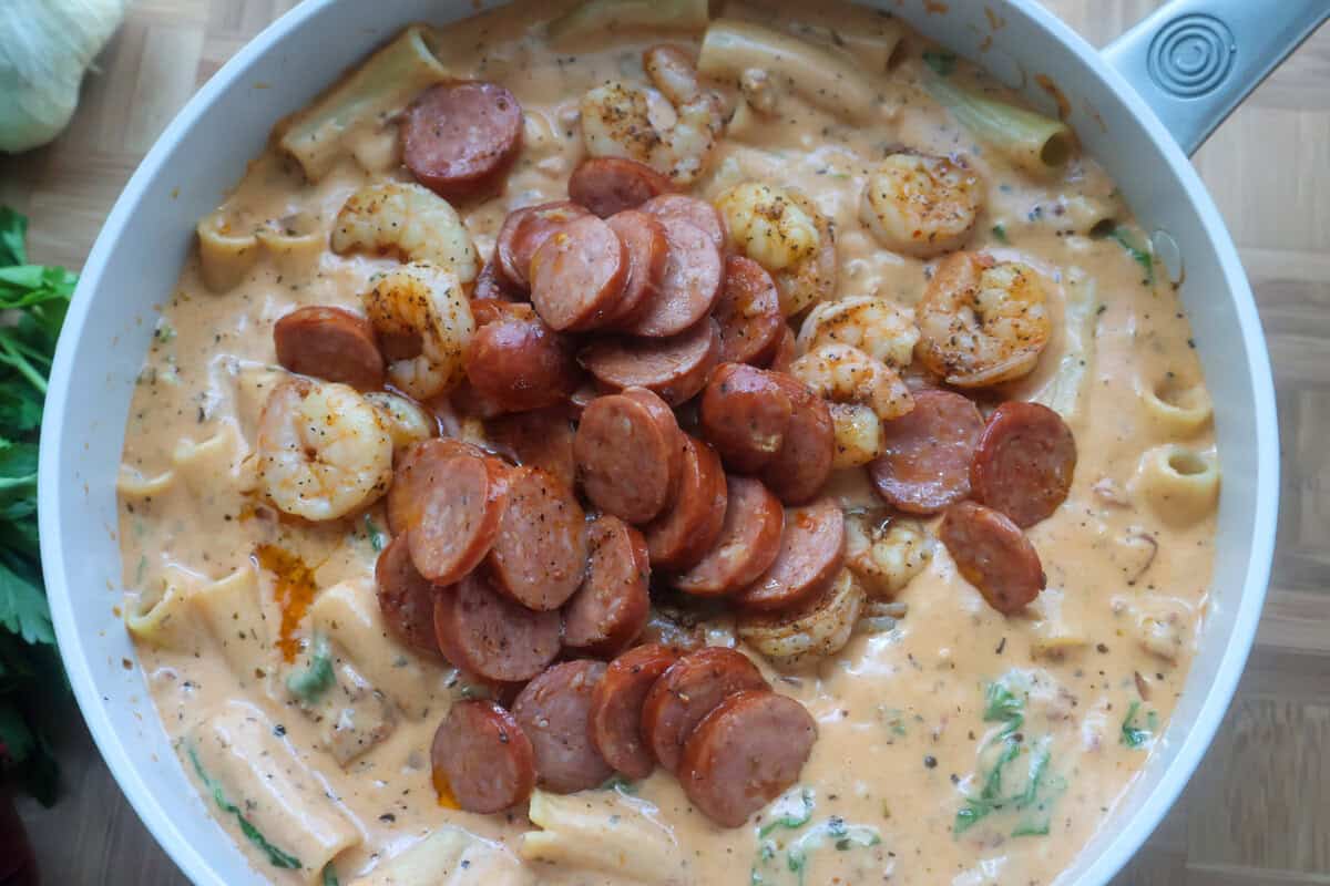 A skillet of cream sauce with sausage on top.